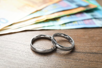 Photo of Silver wedding rings and euro banknotes on wooden table, closeup