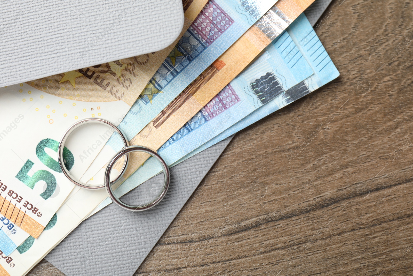Silver wedding rings, envelope and euro banknotes on wooden table, flat lay. Space for text Photo of Silver wedding rings, envelope and euro banknotes on wooden table, flat lay. Space for text