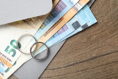 Photo of Silver wedding rings, envelope and euro banknotes on wooden table, flat lay. Space for text