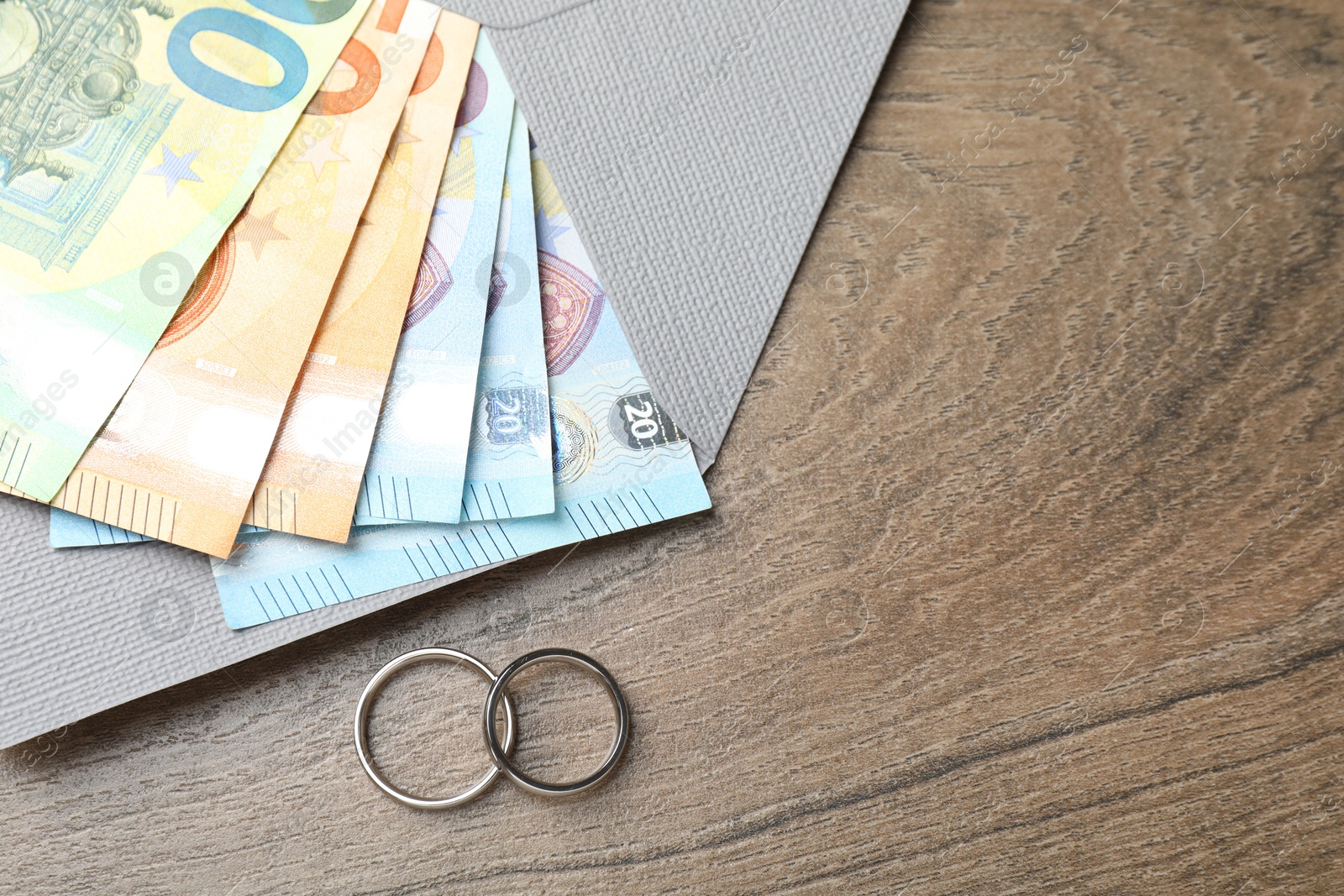Photo of Silver wedding rings, envelope and euro banknotes on wooden table, flat lay. Space for text