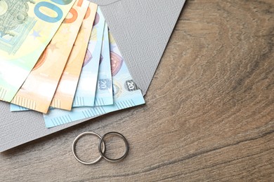 Photo of Silver wedding rings, envelope and euro banknotes on wooden table, flat lay. Space for text