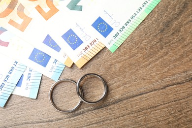 Photo of Silver wedding rings and euro banknotes on wooden table, flat lay. Space for text