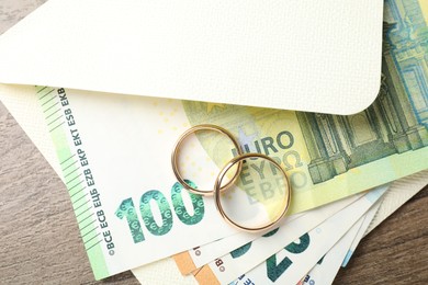 Photo of Gold wedding rings, envelope and euro banknotes on wooden table, flat lay