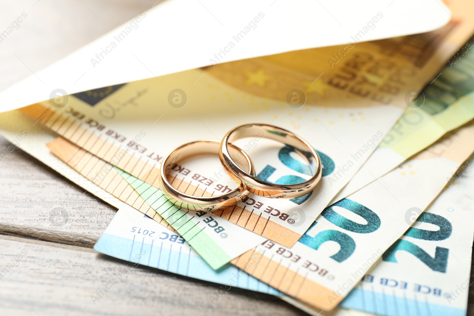 Photo of Gold wedding rings, envelope and euro banknotes on wooden table, closeup