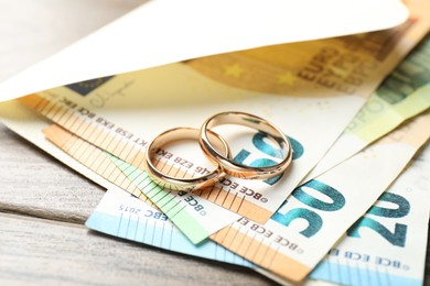 Photo of Gold wedding rings, envelope and euro banknotes on wooden table, closeup