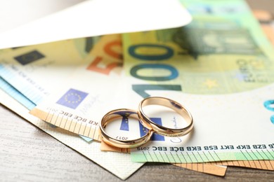 Photo of Gold wedding rings, envelope and euro banknotes on wooden table, closeup