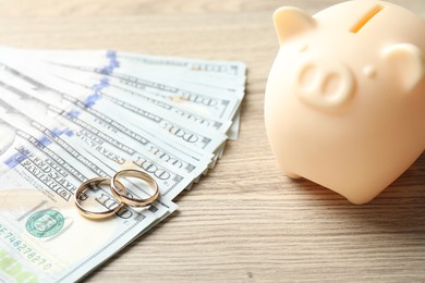 Photo of Gold wedding rings, piggy bank and dollar banknotes on wooden table, closeup