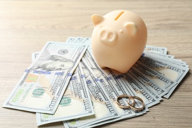 Photo of Gold wedding rings, piggy bank and dollar banknotes on wooden table, closeup