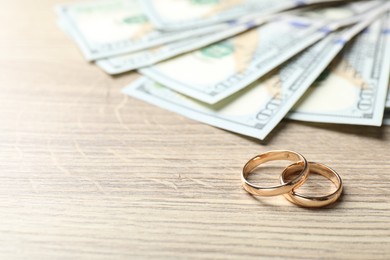 Photo of Gold wedding rings and dollar banknotes on wooden table, closeup. Space for text