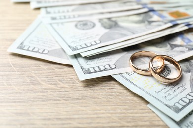 Photo of Gold wedding rings and dollar banknotes on wooden table, closeup. Space for text