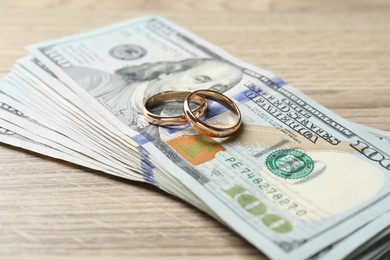 Photo of Gold wedding rings and dollar banknotes on wooden table, closeup