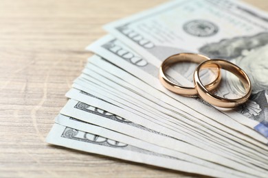 Photo of Gold wedding rings and dollar banknotes on wooden table, closeup