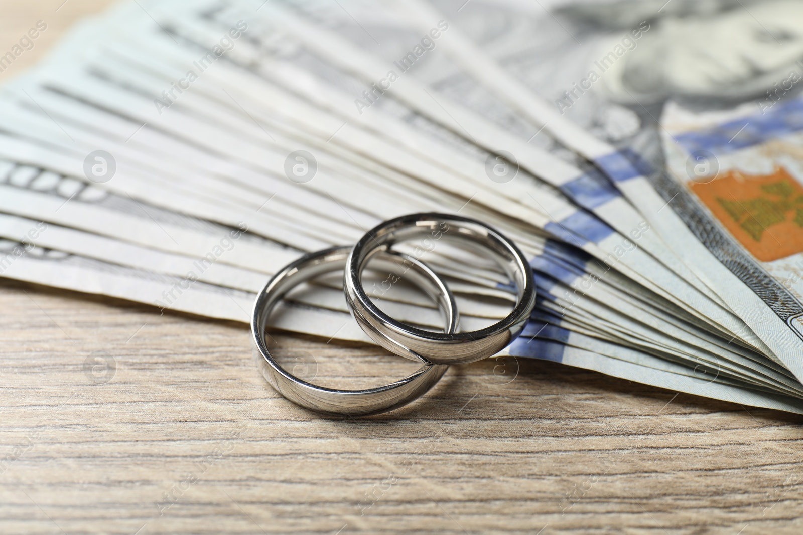 Silver wedding rings and dollar banknotes on wooden table, closeup Photo of Silver wedding rings and dollar banknotes on wooden table, closeup