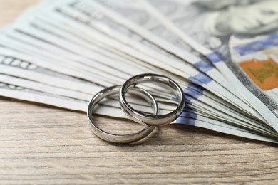 Photo of Silver wedding rings and dollar banknotes on wooden table, closeup