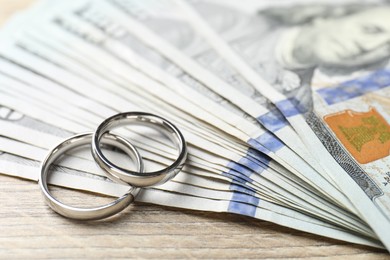 Photo of Silver wedding rings and dollar banknotes on wooden table, closeup