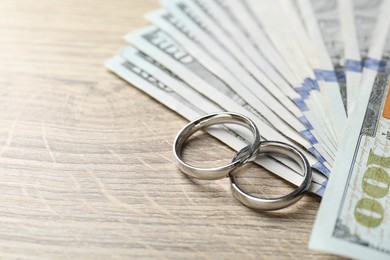 Photo of Silver wedding rings and dollar banknotes on wooden table, closeup. Space for text