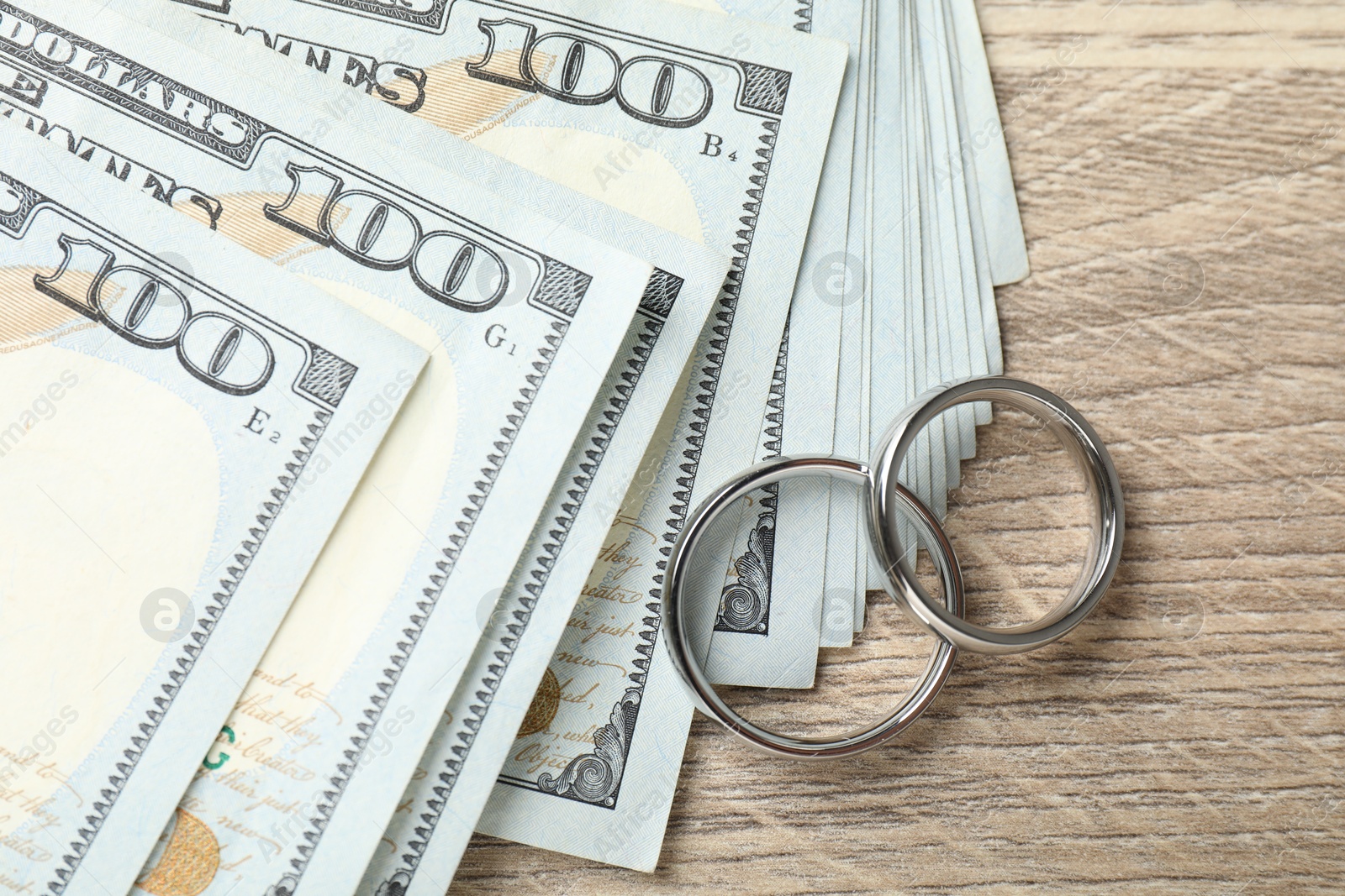 Silver wedding rings and dollar banknotes on wooden table, flat lay Photo of Silver wedding rings and dollar banknotes on wooden table, flat lay