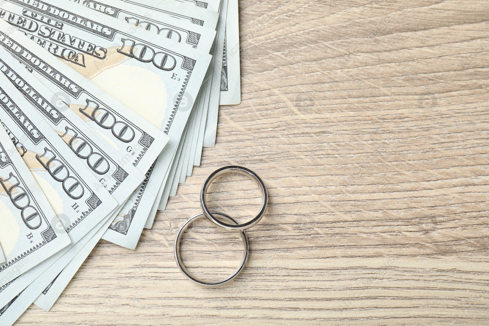 Silver wedding rings and dollar banknotes on wooden table, flat lay. Space for text Photo of Silver wedding rings and dollar banknotes on wooden table, flat lay. Space for text