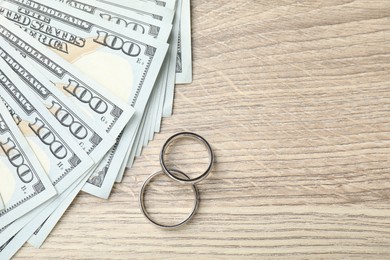 Photo of Silver wedding rings and dollar banknotes on wooden table, flat lay. Space for text