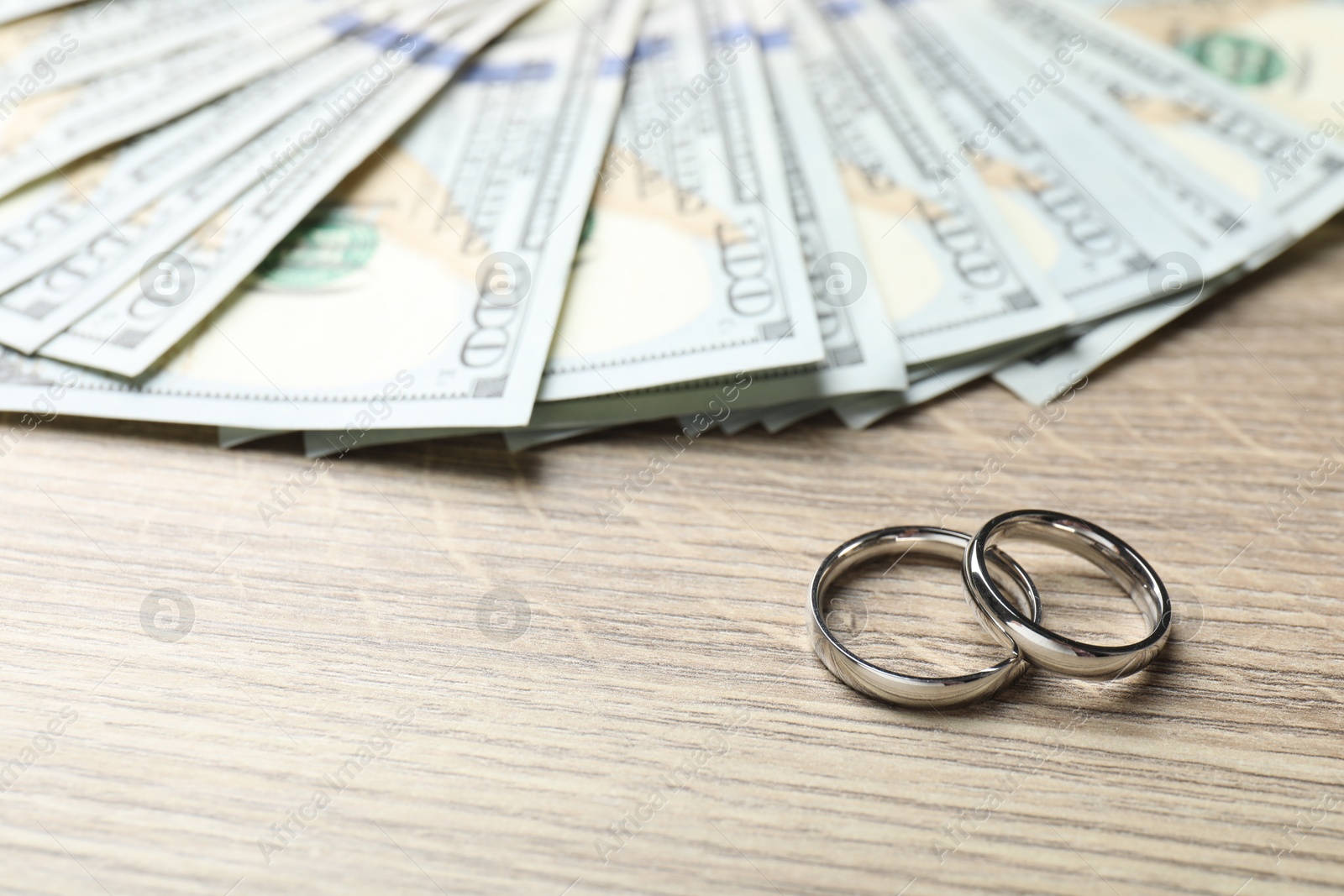 Silver wedding rings and dollar banknotes on wooden table, closeup. Space for text Photo of Silver wedding rings and dollar banknotes on wooden table, closeup. Space for text