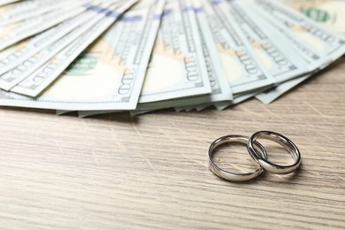 Photo of Silver wedding rings and dollar banknotes on wooden table, closeup. Space for text