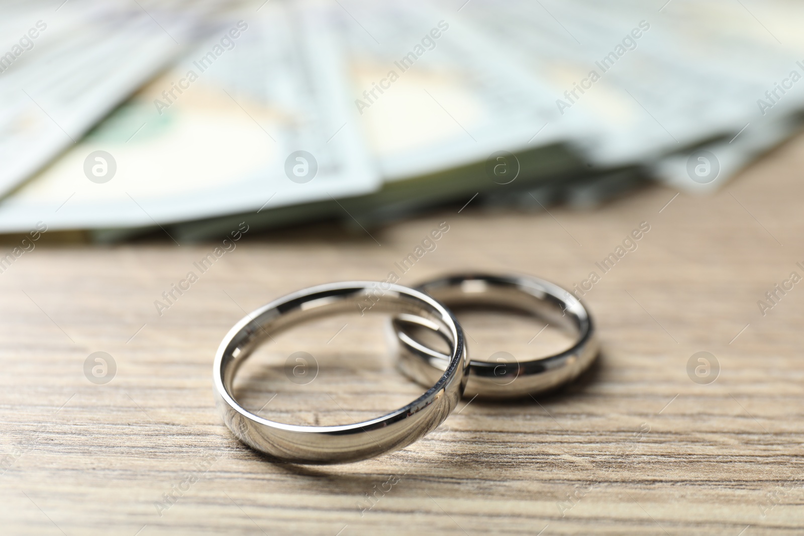 Silver wedding rings and dollar banknotes on wooden table, closeup Photo of Silver wedding rings and dollar banknotes on wooden table, closeup