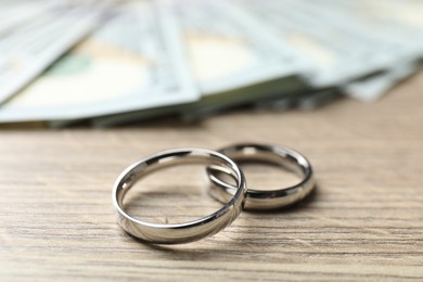 Photo of Silver wedding rings and dollar banknotes on wooden table, closeup