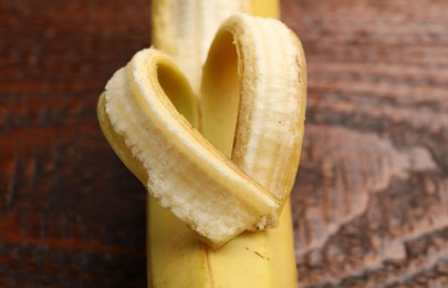 Photo of Banana with heart made of peel on wooden table, closeup