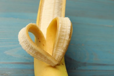 Photo of Banana with heart made of peel on light blue wooden table, closeup