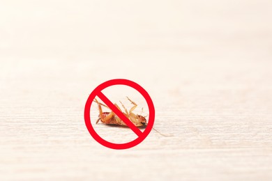 Image of Dead cockroach with red prohibition sign on wooden surface. Pest control