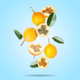 Image of Delicious ripe passion fruits with green leaves falling on light blue background