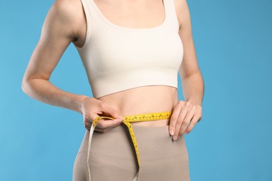 Photo of Beautiful woman measuring her belly with tape on light blue background, closeup