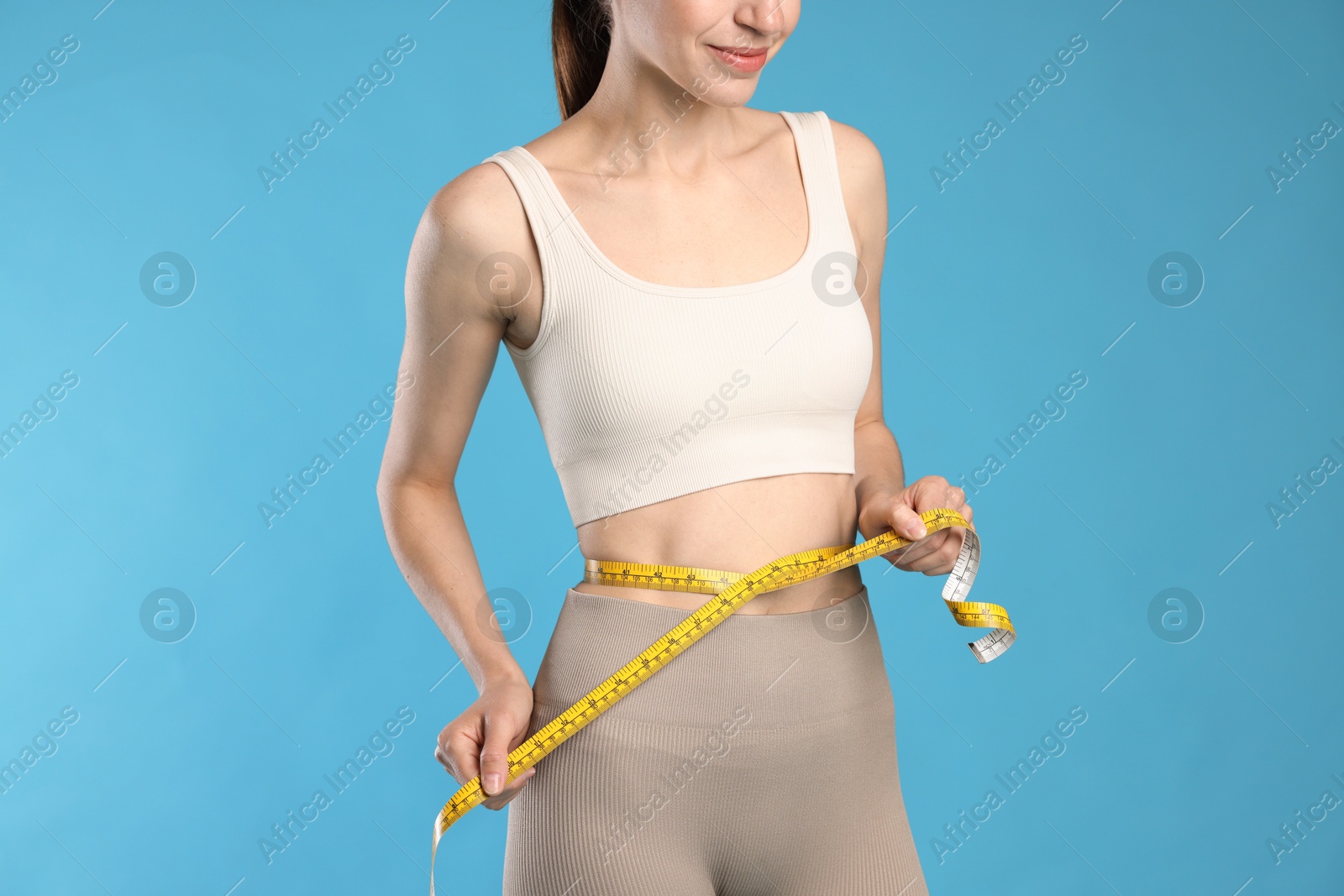 Beautiful woman measuring her belly with tape on light blue background, closeup Photo of Beautiful woman measuring her belly with tape on light blue background, closeup