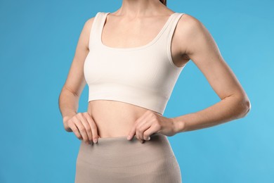 Photo of Beautiful woman with flat belly on light blue background, closeup