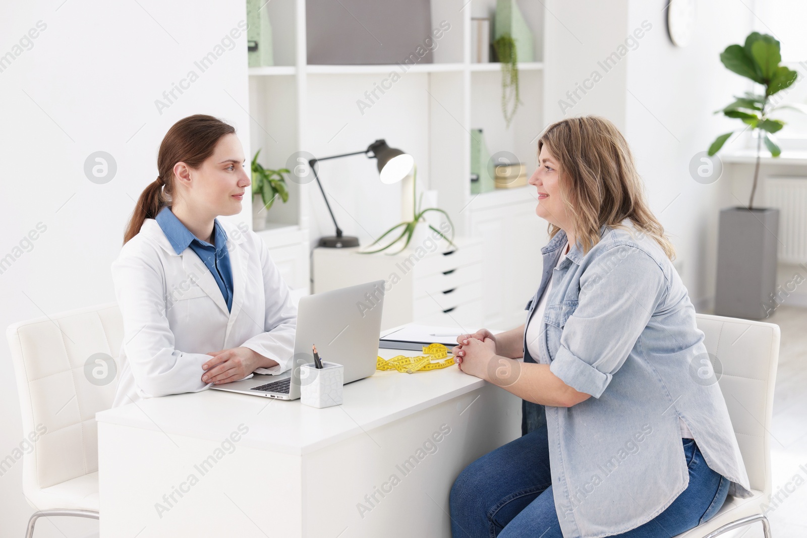 Photo of Weight loss. Nutritionist consulting overweight woman at white desk in clinic