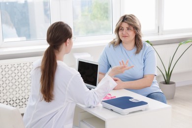 Photo of Weight loss. Nutritionist consulting overweight woman at white desk in clinic