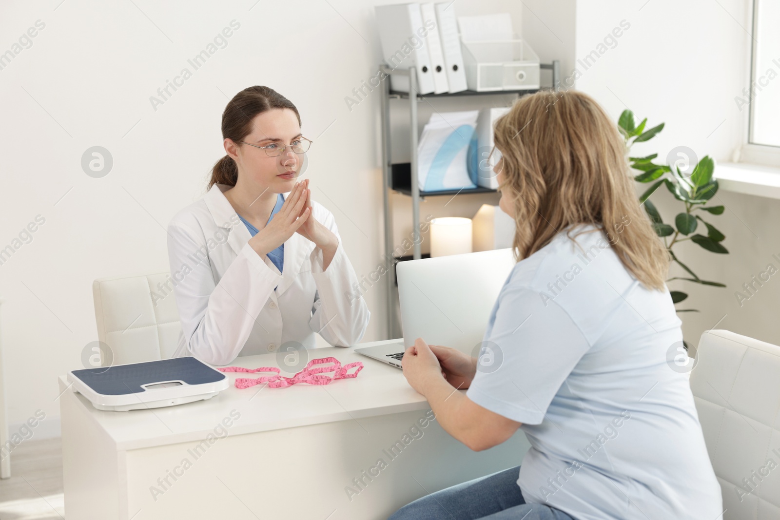 Photo of Weight loss. Nutritionist consulting overweight woman at white desk in clinic