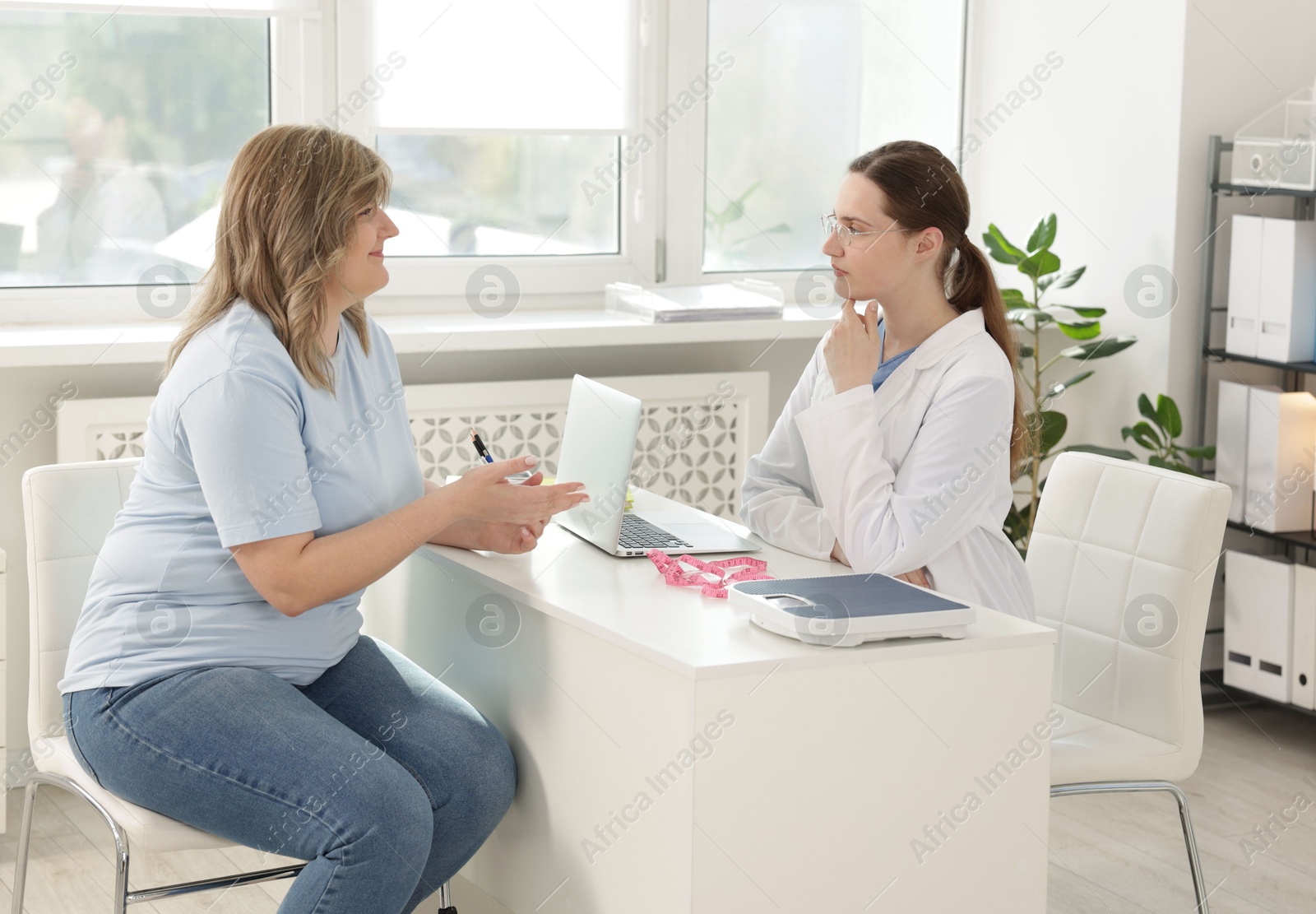 Weight loss. Nutritionist consulting overweight woman at white desk in clinic Photo of Weight loss. Nutritionist consulting overweight woman at white desk in clinic