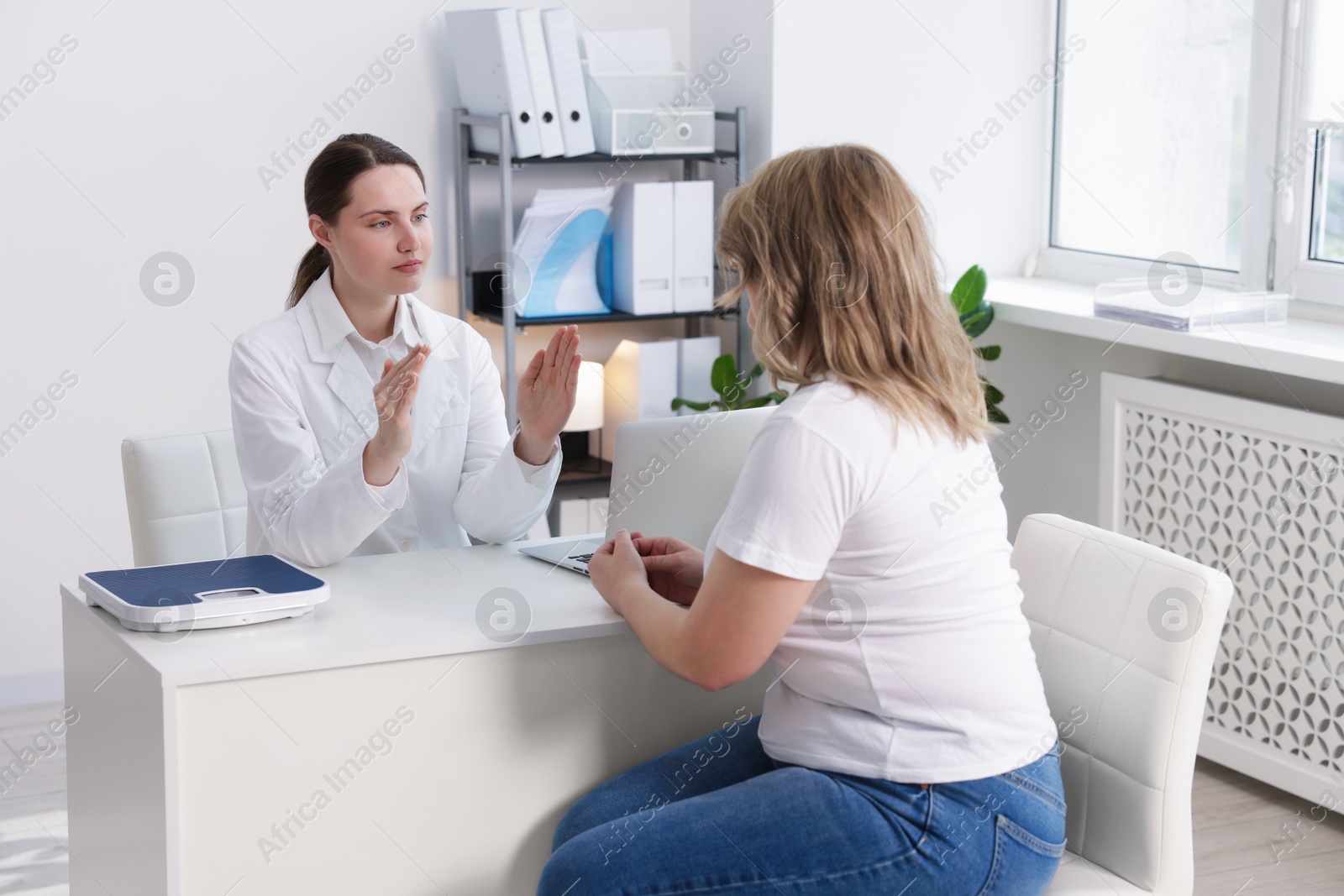 Weight loss. Nutritionist consulting overweight woman at white desk in clinic Photo of Weight loss. Nutritionist consulting overweight woman at white desk in clinic