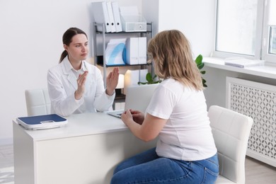 Photo of Weight loss. Nutritionist consulting overweight woman at white desk in clinic