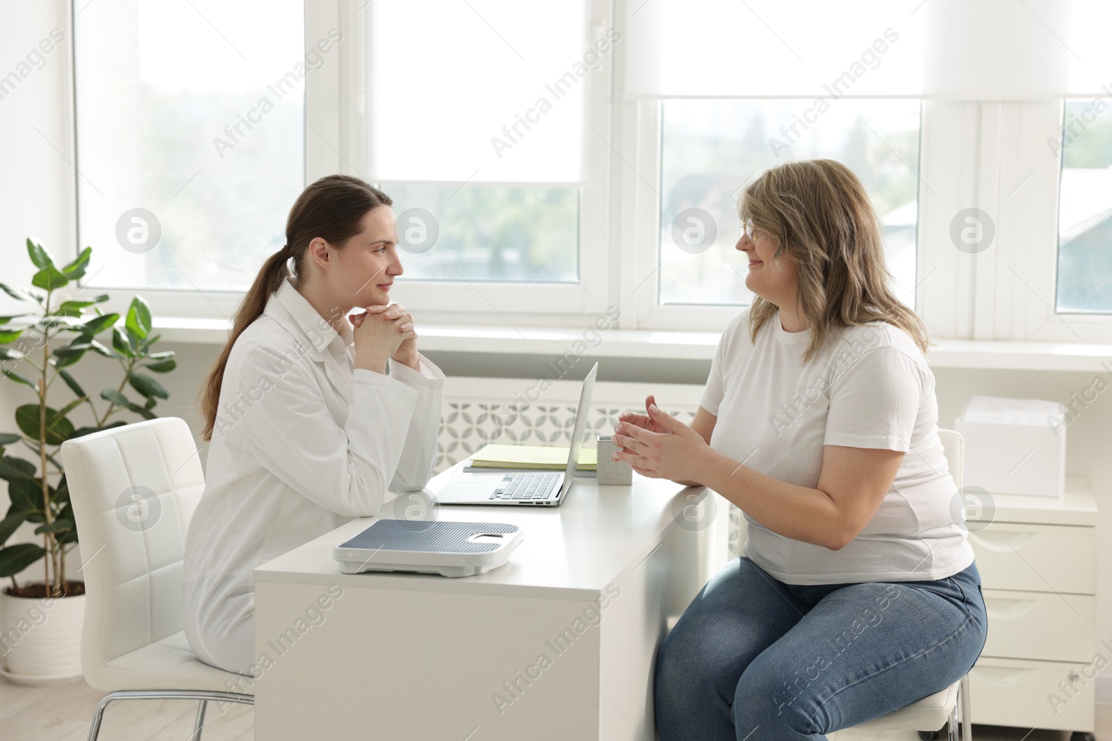 Weight loss. Nutritionist consulting overweight woman at white desk in clinic Photo of Weight loss. Nutritionist consulting overweight woman at white desk in clinic