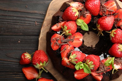 Photo of Delicious bundt cake with strawberries, mint and chocolate shavings on wooden table, flat lay