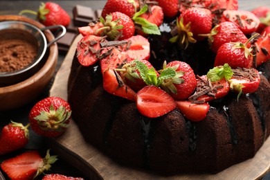 Photo of Delicious bundt cake with strawberries, mint and chocolate shavings on table, closeup