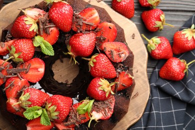 Photo of Delicious bundt cake with strawberries, mint and chocolate shavings on wooden table, flat lay