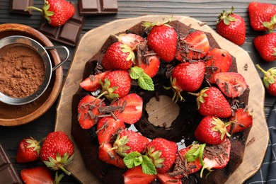 Photo of Delicious bundt cake with strawberries, mint and chocolate shavings on wooden table, flat lay