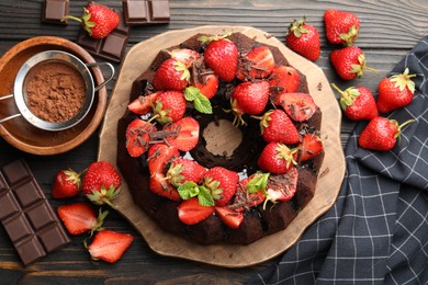 Photo of Delicious bundt cake with strawberries, mint and chocolate shavings on wooden table, flat lay