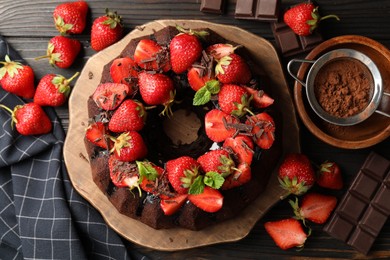 Photo of Delicious bundt cake with strawberries, mint and chocolate shavings on wooden table, flat lay