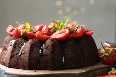 Photo of Delicious chocolate bundt cake with strawberries and mint on board against grey background, closeup