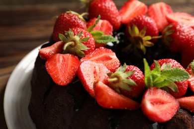 Photo of Delicious chocolate bundt cake with strawberries and mint on wooden table, closeup