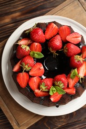 Photo of Delicious chocolate bundt cake with strawberries and mint on wooden table, top view